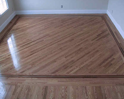 Wooden floor with a diagonal pattern and a dark border trim, set in a square room with beige walls and white baseboards.