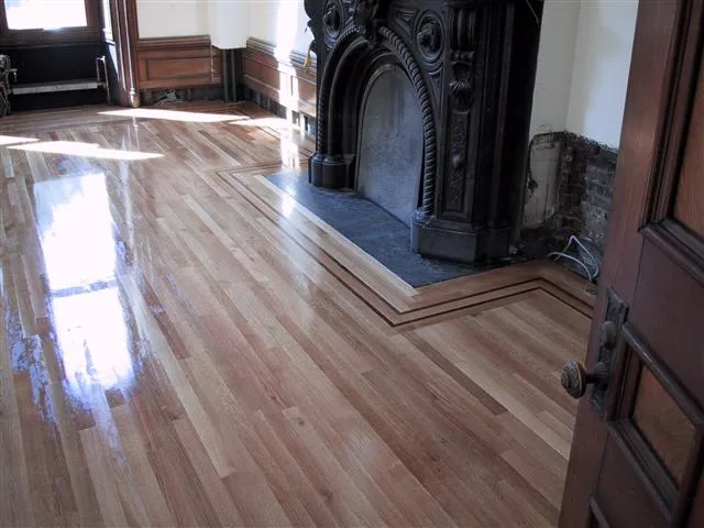 Room with polished wooden floor, dark ornate fireplace, and partially visible door in the foreground.