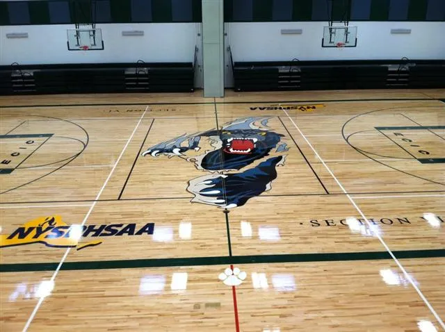 Indoor basketball court with a fierce wolf graphic at center, surrounded by black lines and NYSPHSAA logo on the hardwood floor.